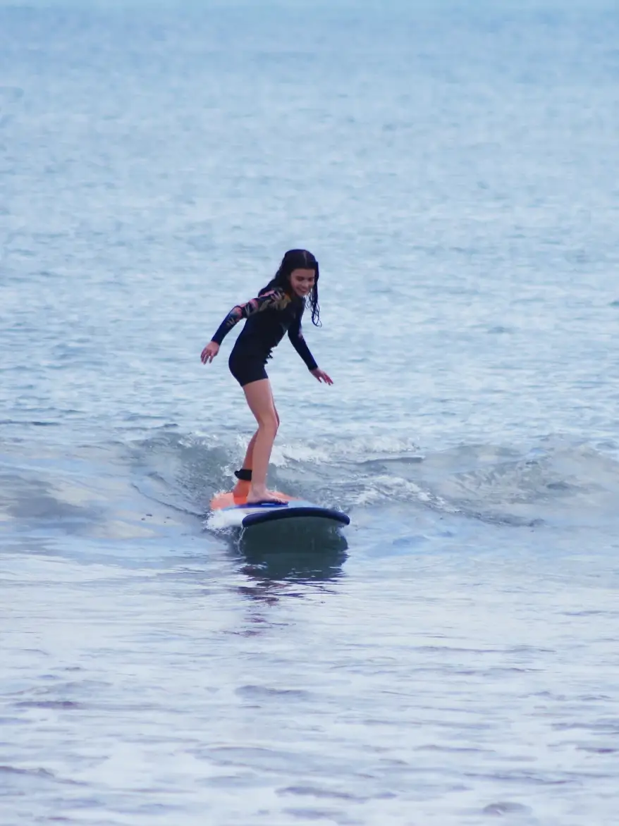 A young surfer riding a soft-top surfboard across a small green wave in Bali