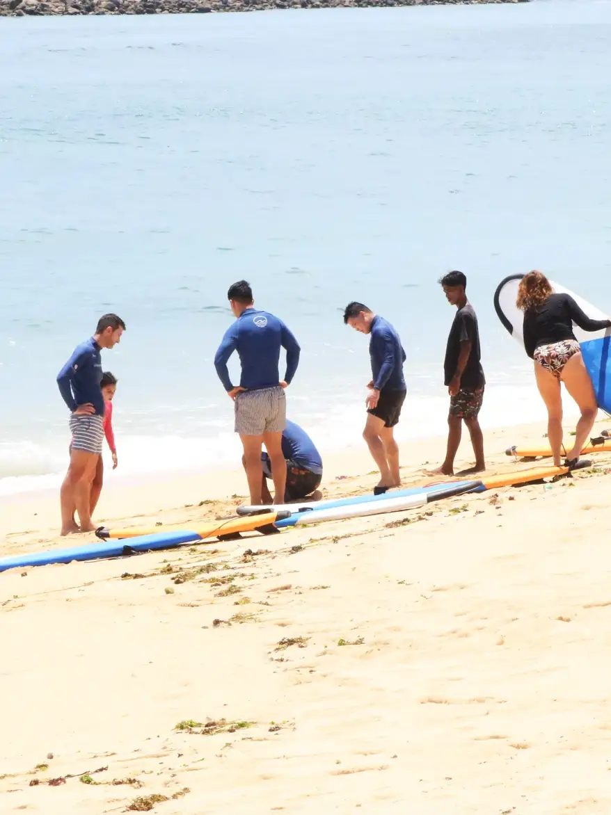 A group of surfers standing with their boards on a white sand beach in Bali before a lesson