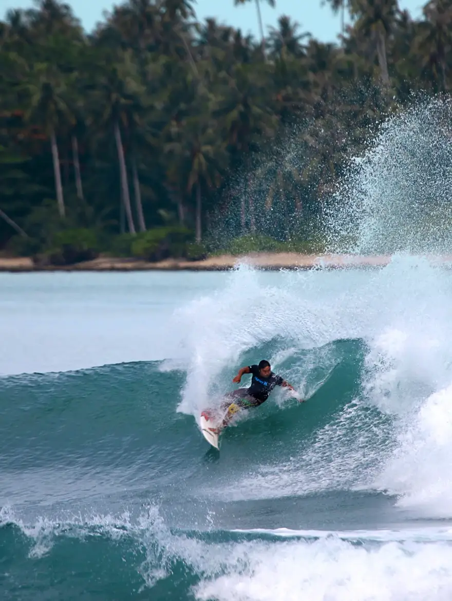 Justin Buu’lolo hitting the lip of a wave in front of palm trees in Nias