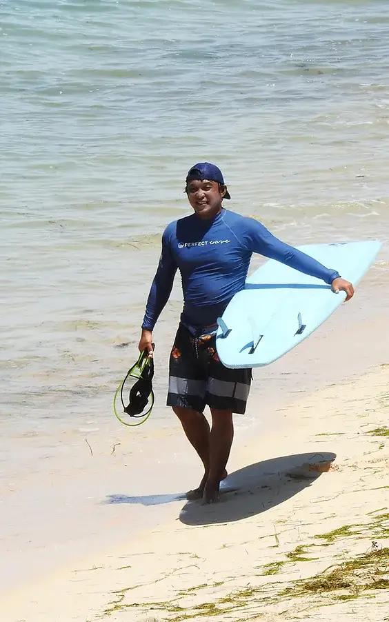 Justin Buu’lolo walking out of the water in Bali carrying a soft-top surfboard